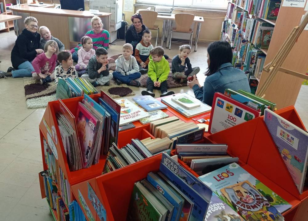 Dzieci słuchają pani bibliotekarki, która opowiada im o bibliotece.
