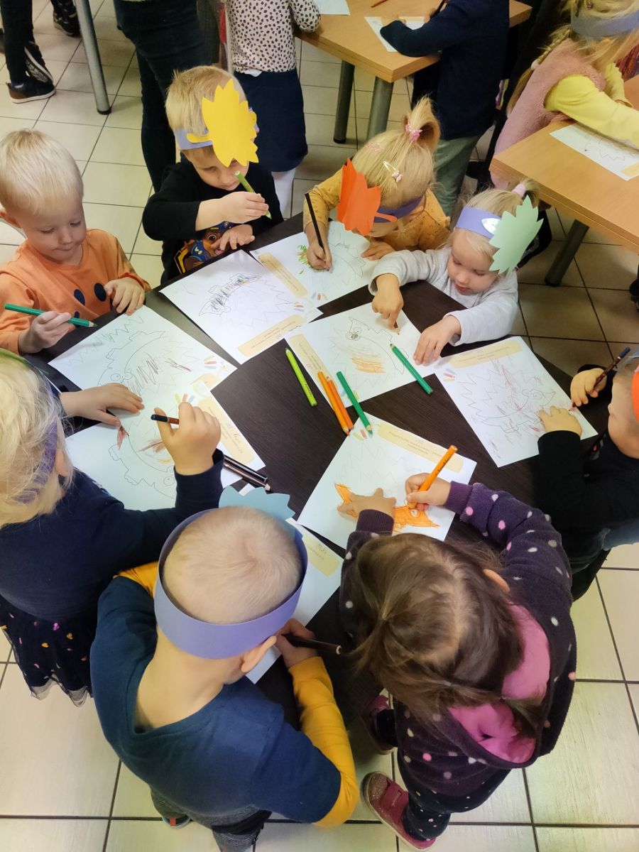 Przedszkolaki przy stoliku kolorują obrazki jesienne.