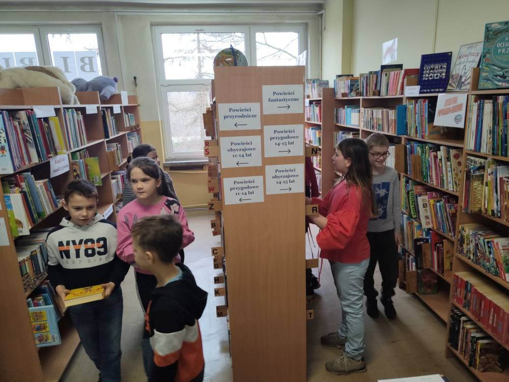 Uczniowie wybierają sobie książki z półek bibliotecznych.